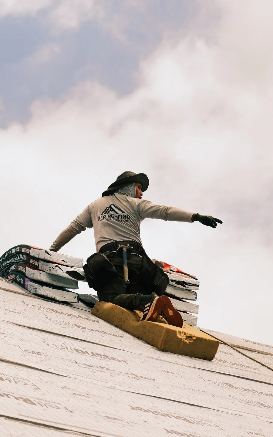 R&R Roofing crew member on a roof deck beside stacked GAF shingle bundles during an installation